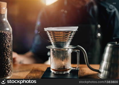 Close up Kalita Wave Dripper on black digital scale, wooden table. Tools and equipment for making Drip Brew coffee. Barista with tattooed arms wearing dark uniform.