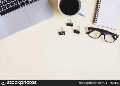 close up laptop tea cup paperclip eyeglasses spiral notepad beige backdrop