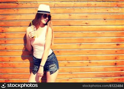 Close up lifestyle fashion portrait of woman posing on the street drinking smoothie, wearing stylish outfit and sunglasses, summer hat, joy, relax, vacation.