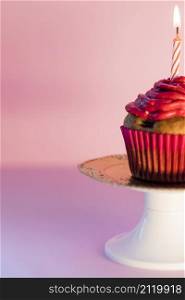 close up lighted candle cupcake cakestand against pink background