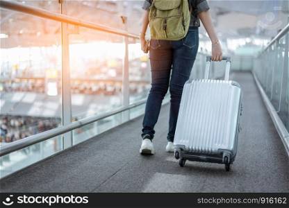 Close up lower body of woman traveler with luggage suitcase going to around the world by plane. Female tourist on automatic escalator in airport terminal.