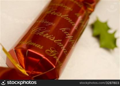Close up macro shot of a Christmas cracker with a holly leaf in the background.