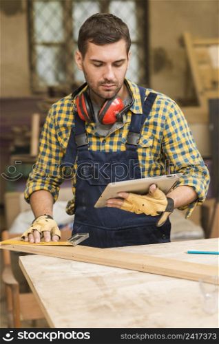 close up male carpenter looking digital tablet measuring wooden block