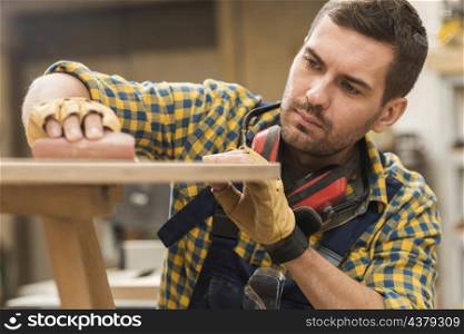 close up male carpenter rubbing sand paper wooden surface