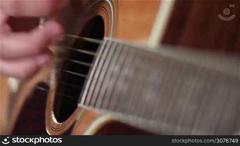 Close up male hands on strings playing classic acoustic guitar. Guitarist performing chords while jamming in recording studio.