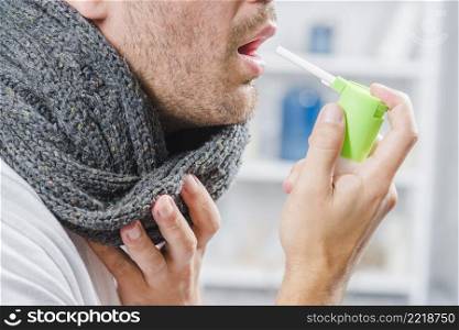 close up man wearing gray scarf around his neck using spray treat sore throat