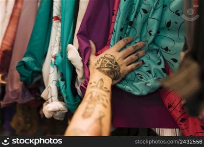 close up man with tattoo his hand touching shirts arranged rail