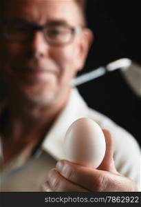 Close up, mature man golfer wearing a white shirt and he holds a white egg on hand, iron golf club on his shoulder - focus on ball, studio shot, black background