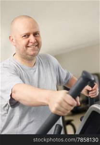 Close up, mature man takes care of his health and he use elliptical trainer in the gym