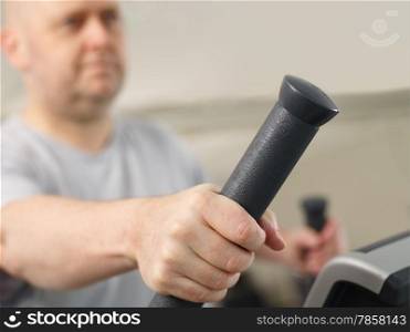 Close up, mature man takes care of his health and he use elliptical trainer in the gym - focus on a hand