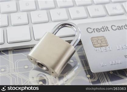 Close up metal padlock with silver credit card reflecting shadow on digital circuits and modern white keyboard on background. Online payment, banking data protection, security financial concepts.