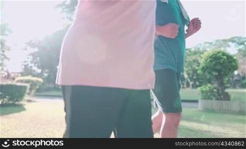 close up mid body elder couple jogging together inside the park on hot sunny morning, family get together, healthy activities, human aging process, active retirement lifestyle, warm morning light