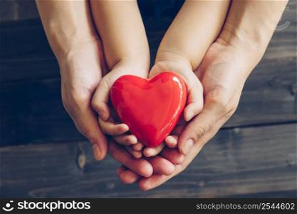 Close up mother and children hands giving red heart on wood background