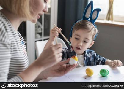 close up mother showing little boy how paint eggs