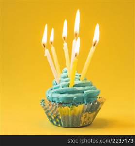 close up muffin with burning candles yellow background