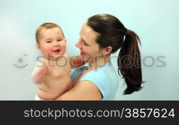Close-up of a baby boy grabbing and kissing his mother against a light blue wall