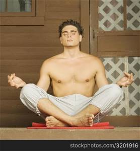 Close-up of a bare chested young man sitting in a lotus position and meditating