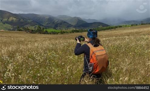 Close up of a beautiful Hispanic female scout seen from behind with a backpack taking a picture in the middle of a sown field on a cloudy morning. Close up of a beautiful Hispanic female scout seen from behind with a backpack taking a picture in the middle of a sown field