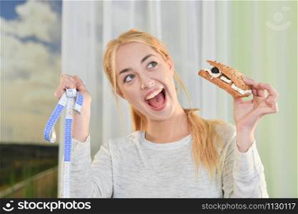 Close-up of a blonde Woman looks happy while holding a sandwich and a measuring tape on an out of focus background. Healthy lifestyle concept.. Woman happy after checking her weight loss