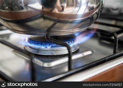 Close up of a blue gas flame, cooking a water pot in kitchen