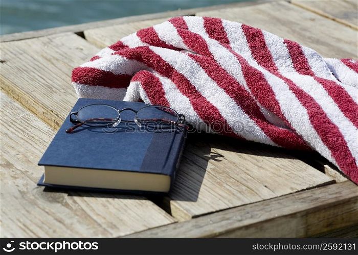 Close-up of a book and a pair of eyeglasses with a towel on a jetty