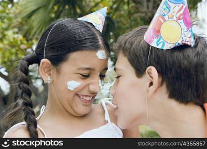 Close-up of a boy and his sister balancing a cake between their noses
