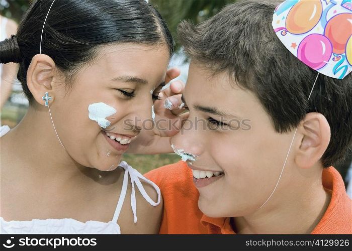 Close-up of a boy and his sister smiling with cake on their faces