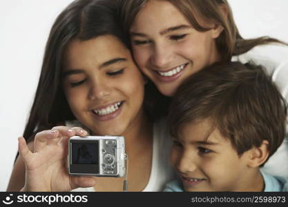 Close-up of a boy and his two sisters taking a photograph of themselves with a digital camera