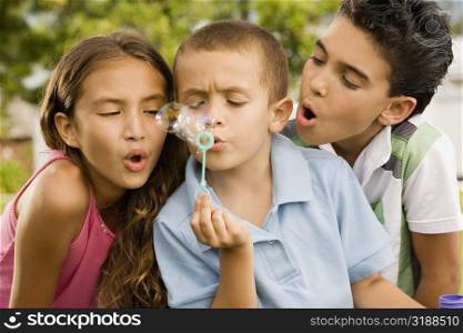 Close-up of a boy blowing bubbles with a girl and a boy beside him
