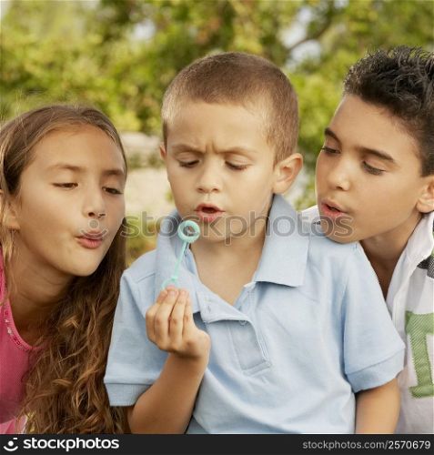 Close-up of a boy blowing bubbles with his brother and sister