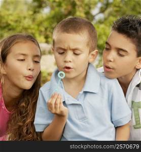 Close-up of a boy blowing bubbles with his brother and sister