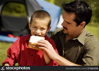 Close-up of a boy eating a sandwich with his father