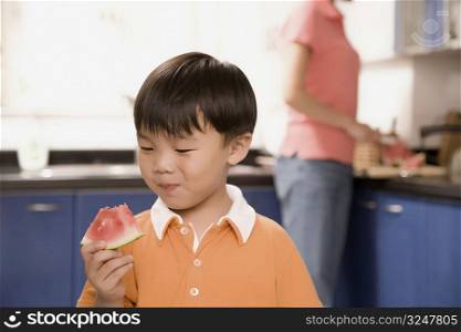 Close-up of a boy eating watermelon with his mother standing behind him