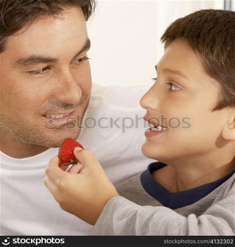 Close-up of a boy feeding his father a strawberry