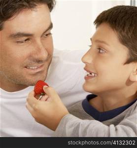Close-up of a boy feeding his father a strawberry