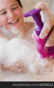 Close-up of a boy holding a soap dispenser in a bathtub