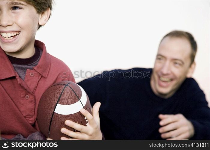Close-up of a boy holding an American football with a mid adult man in the background
