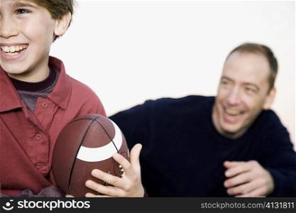 Close-up of a boy holding an American football with a mid adult man in the background
