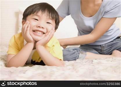 Close-up of a boy leaning on his elbows and her mother sitting near him