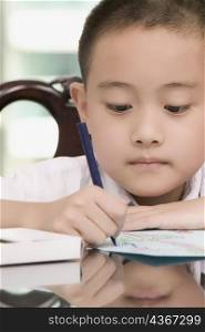 Close-up of a boy looking down and writing on a sheet of paper