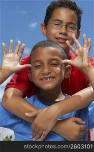 Close-up of a boy making a face with his friend hugging him from behind