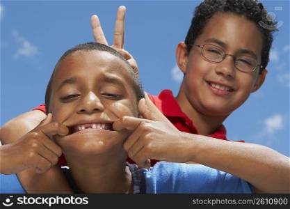 Close-up of a boy making a face with his friend making a gesture of rabbit ears from behind