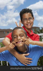 Close-up of a boy making a face with his friend making a gesture of rabbit ears from behind