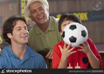 Close-up of a boy playing with a soccer all with his father and grandfather smiling