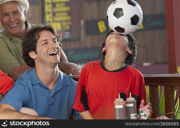 Close-up of a boy playing with a soccer ball with his father and grandfather beside him