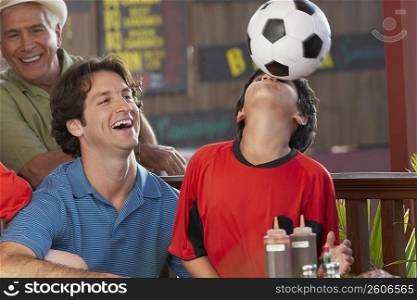 Close-up of a boy playing with a soccer ball with his father and grandfather beside him