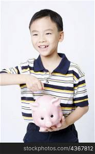 Close-up of a boy putting a coin into a piggy bank