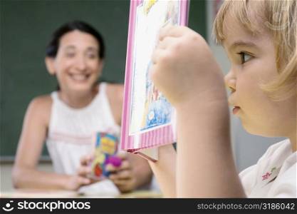 Close-up of a boy reading a book with his teacher sitting beside him