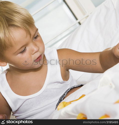 Close-up of a boy sitting on the bed playing with rose petals