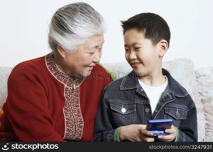 Close-up of a boy sitting with his grandmother holding a video game console